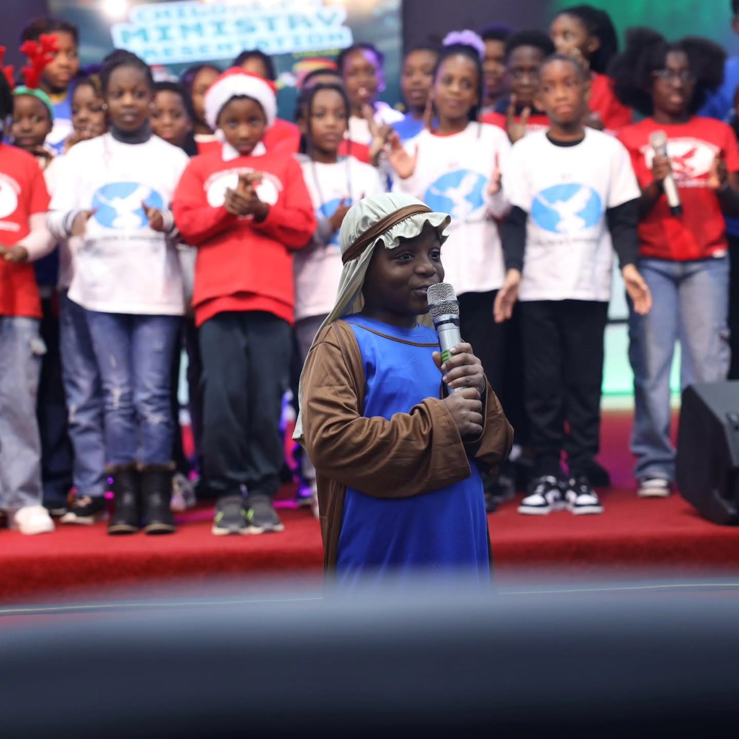 A young boy in nativity costume singing into a microphone at the children's Christmas presentation