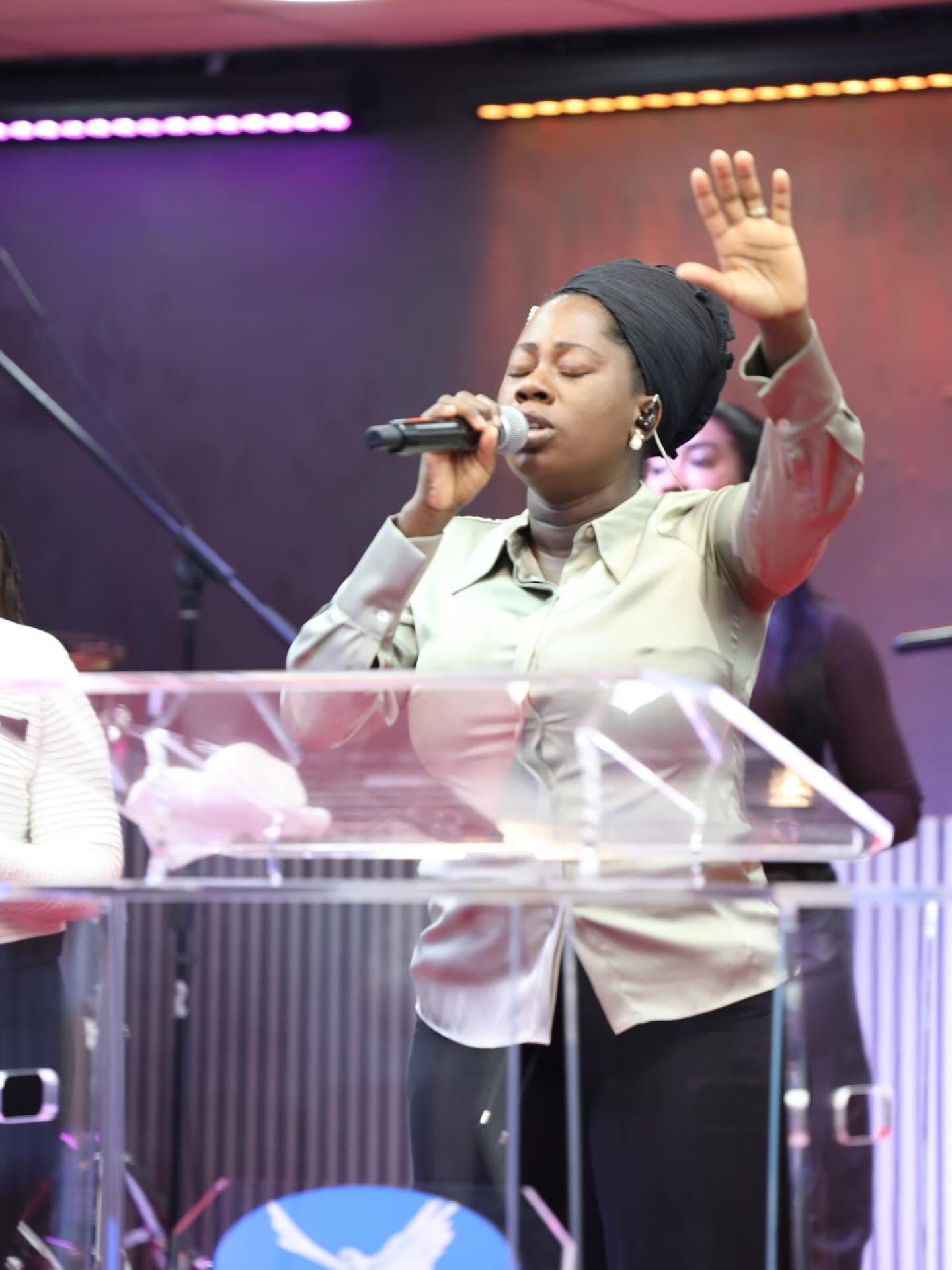 A worship leader singing with one hand lifted at the pulpit